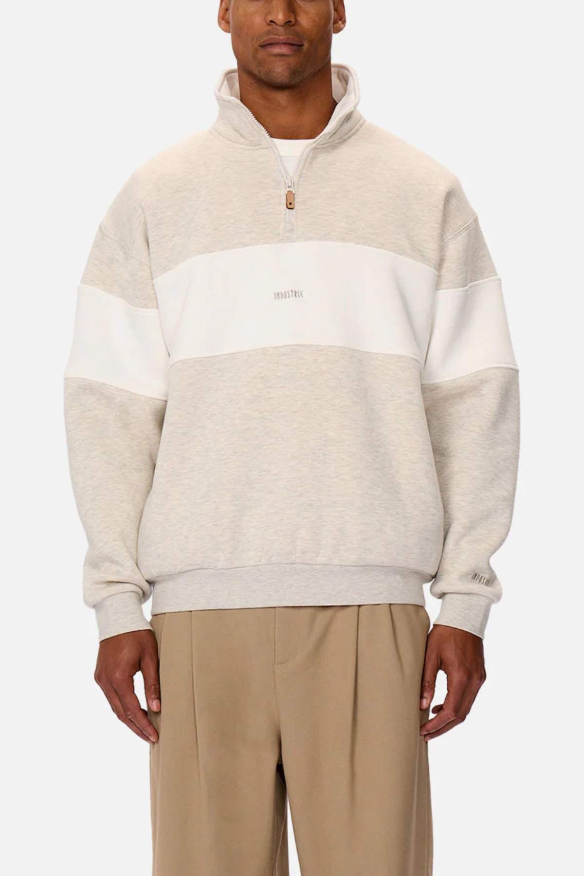 Wearing the Industrie The Luton Track Top, featuring a light gray quarter zip neck, white chest stripe, and beige pants. This pullover has subtle front text and a soft fleece lining against a plain white background.