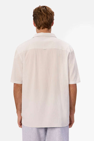 Rear view of a person wearing an oversized fit, light beige Industrie The Magna Short Sleeve Shirt paired with light gray pants. Made from 100% cotton, the fabric's texture stands out against a plain white background.