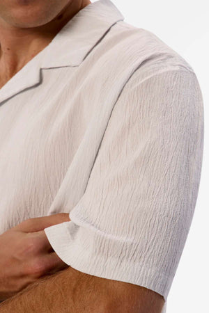 A close-up shows someone wearing the Industrie The Magna Short Sleeve Shirt, crossing their arms. The shirt is 100% cotton with a textured design, focusing on its fabric and sleeve detail. Its oversized fit provides relaxed style against a plain white background.