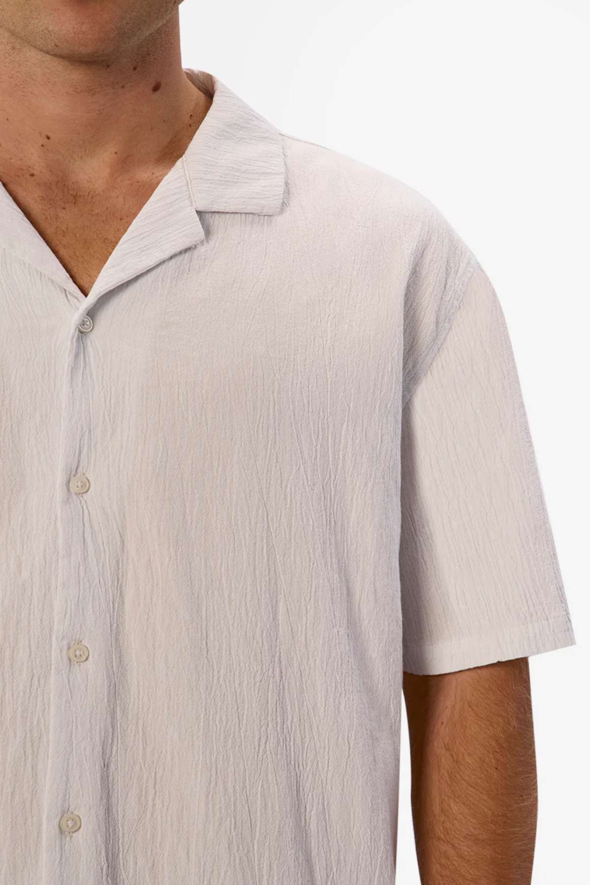 A man in an Industrie The Magna Short Sleeve Shirt, made of 100% cotton, stands against a white background. The focus is on his upper right side, showcasing the shirt’s texture and collar. His face remains out of frame.