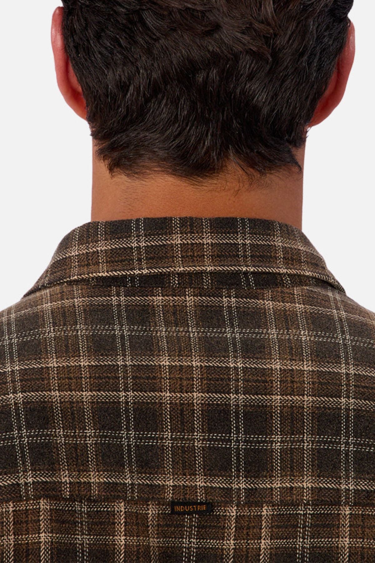 A close-up shows the back of a person with short dark hair wearing the Industrie The Maple Long Sleeve Shirt, featuring a brown checked pattern and a small "INDUSTRIE" label on the collar.