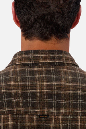 A close-up shows the back of a person with short dark hair wearing the Industrie The Maple Long Sleeve Shirt, featuring a brown checked pattern and a small "INDUSTRIE" label on the collar.