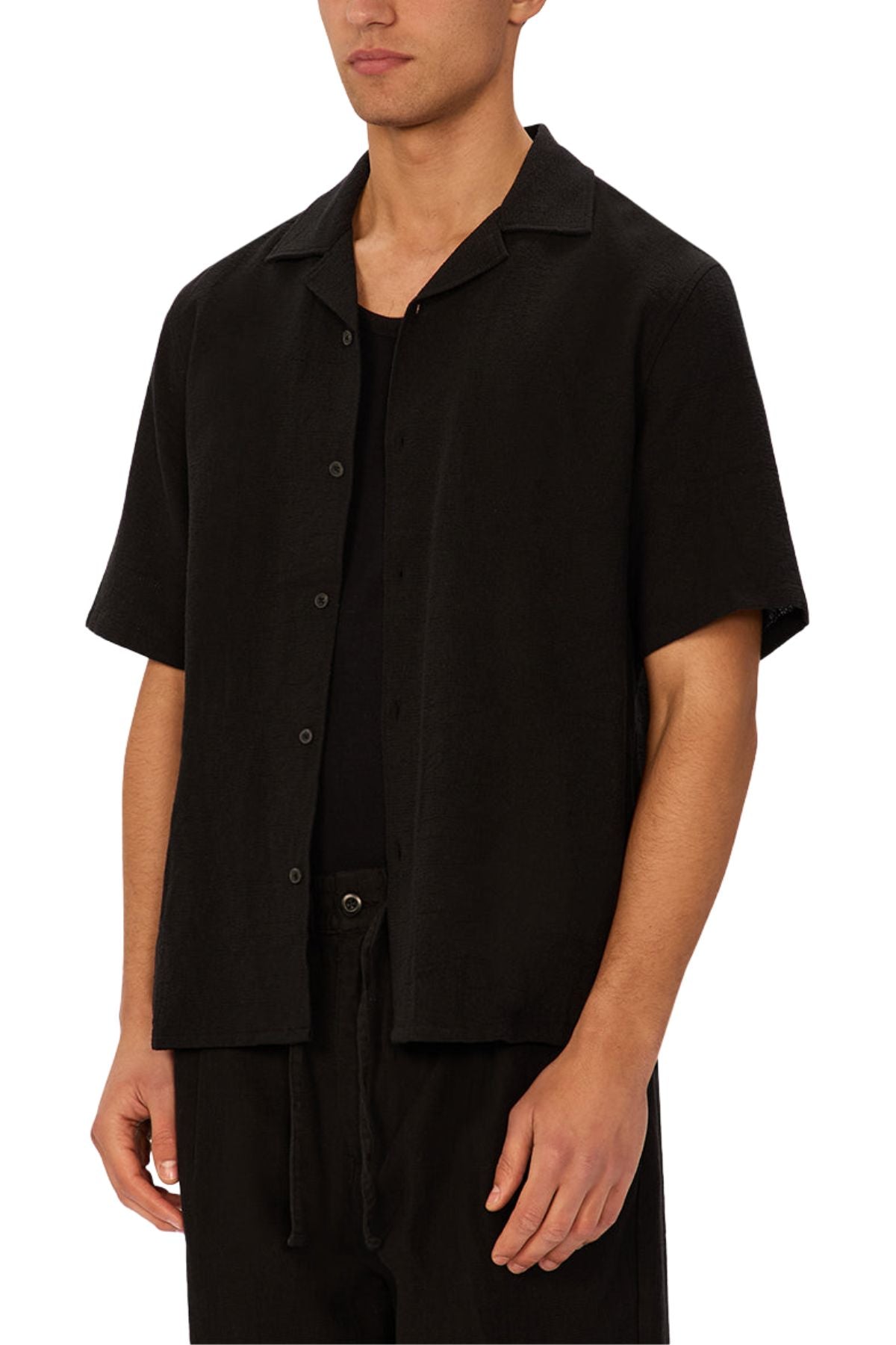 A man wears the Industrie The Marbella Short Sleeve Shirt over a black t-shirt and black pants, standing with arms relaxed at his sides against a plain white background.