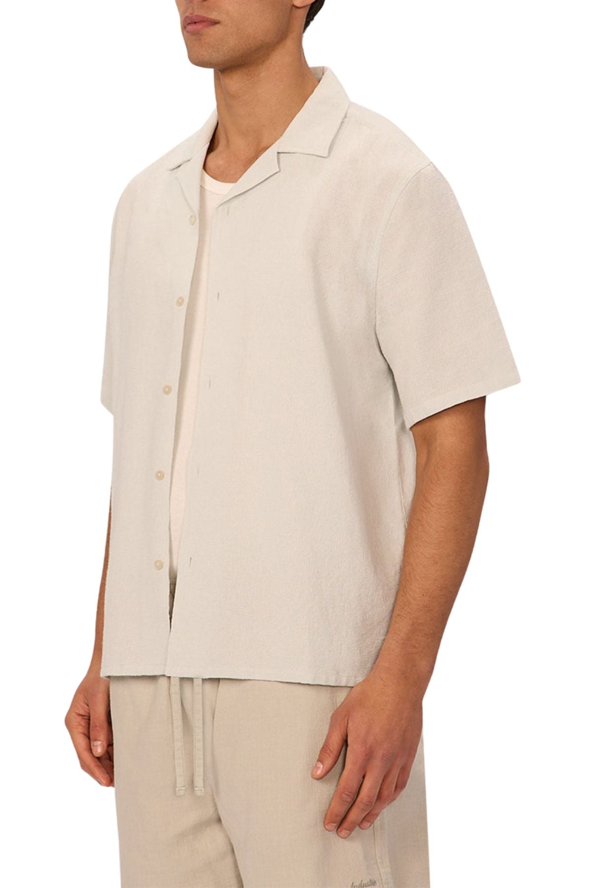 A man in the Industrie The Marbella Short Sleeve Shirt, a relaxed fit lightweight textured shirt, worn over a white tee with matching beige drawstring pants, stands against a plain white background.