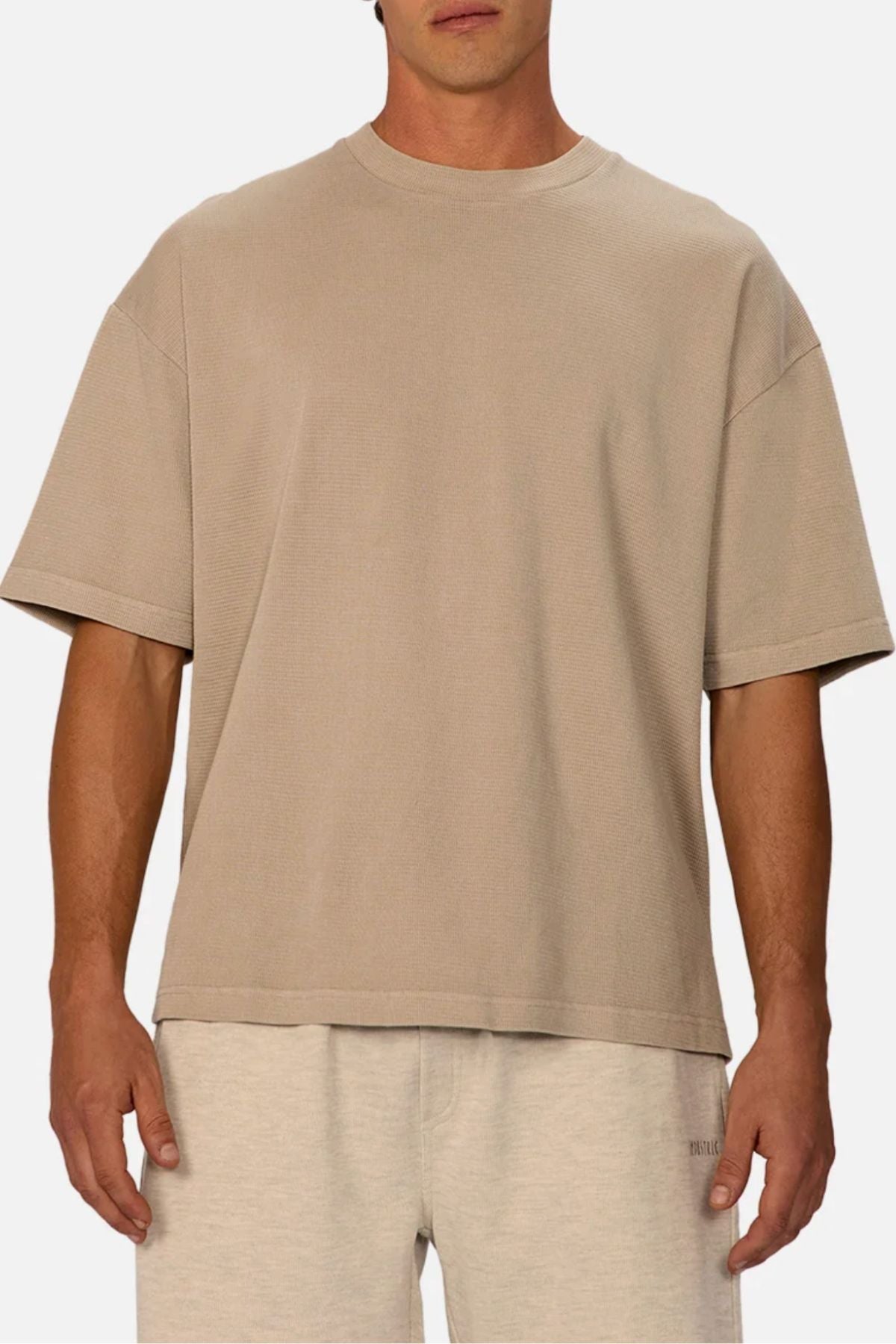 A man stands facing forward in the Industrie The Marlon Tee, a relaxed fit beige tee, paired with light grey shorts against a plain background for an effortless casual look.