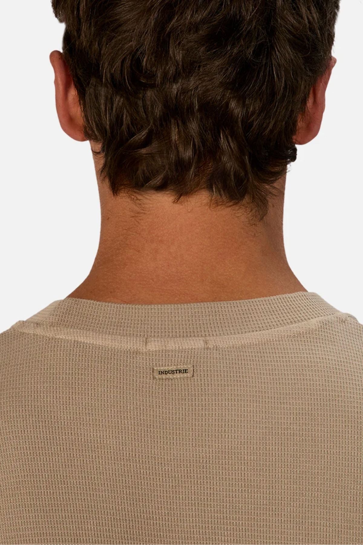 The image features the back view of a person wearing the Industrie The Marlon Tee, a beige waffle knit shirt with a small "INDUSTRIE" label below the collar. The plain white background highlights this stylish, casual top.