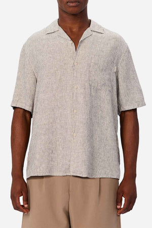 A man wears the Industrie The Melrose Short Sleeve Shirt in light gray with a collar and chest pocket, paired with loose beige pants, standing against a plain white background.