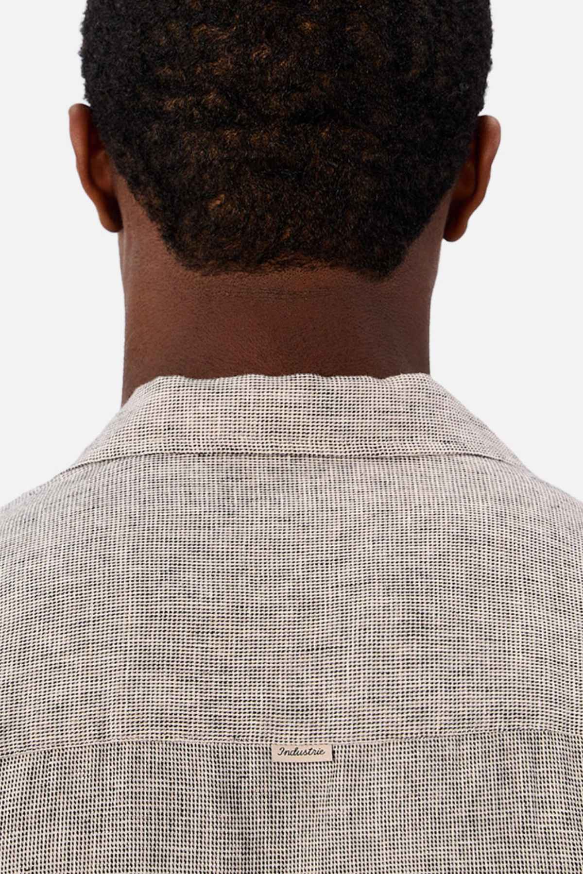 A person with short, curly hair is shown from behind wearing a light gray Industrie The Melrose Short Sleeve Shirt featuring a small tag at the upper back, set against a plain white background.