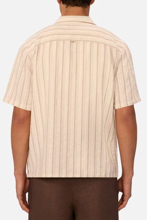 A person is seen from behind wearing the Industrie The Miramar Short Sleeve Shirt, featuring cream fabric with thin red and beige vertical stripes, a collar, and short sleeves—styled casually with brown pants.