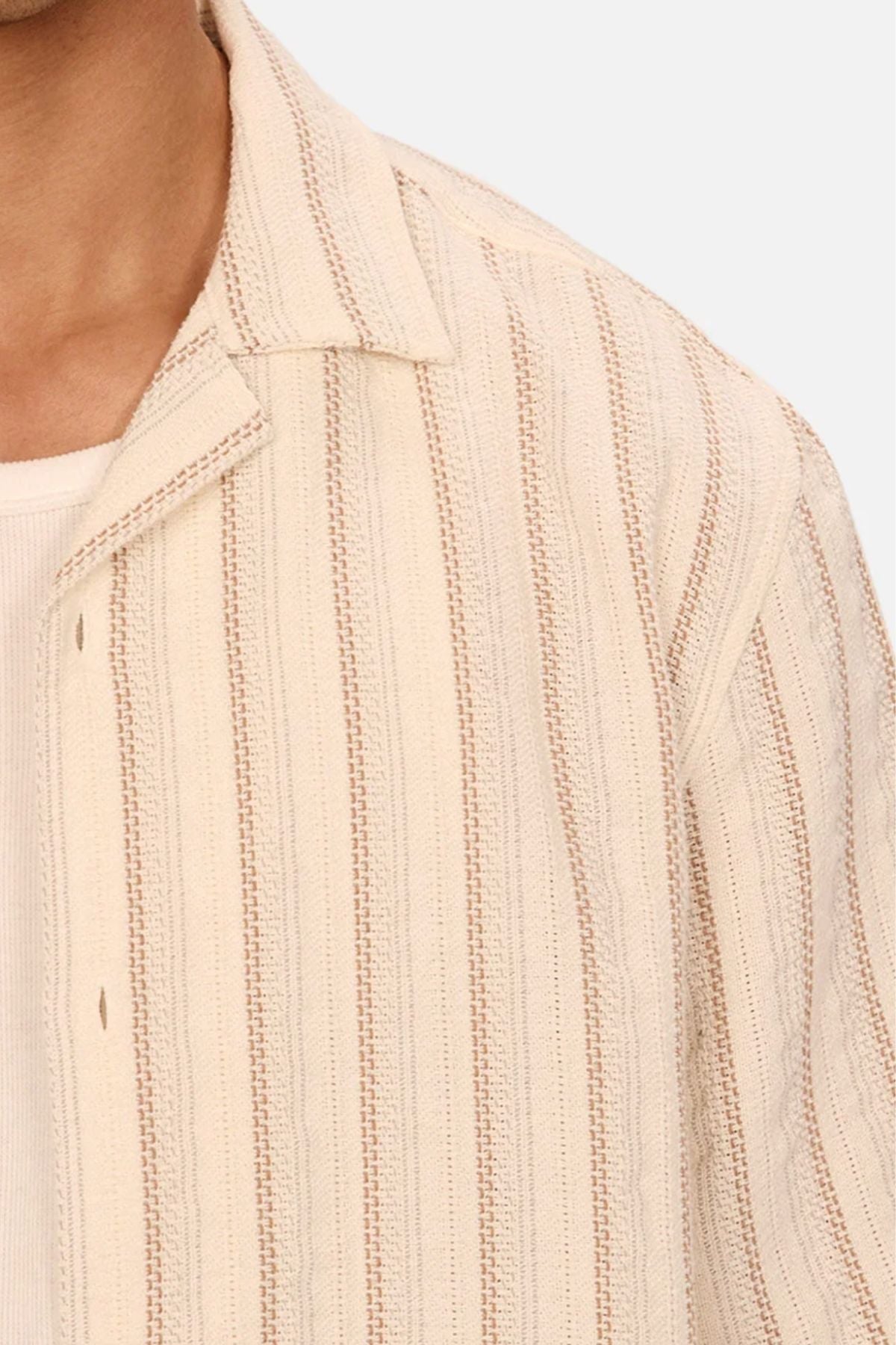 A close-up shows the shoulder and chest of a person wearing the Industrie The Miramar Short Sleeve Shirt—a cream, vertical-stripe, textured style—layered over a light ribbed top for an understated casual look.
