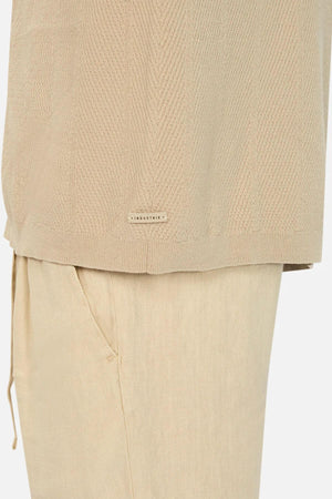 Close-up of a person in the Industrie The Modena Short Sleeve Shirt, a beige textured design with a camp collar, paired with matching pants. The shirt displays an "INDUSTRIE" label. Pants feature visible side pocket and drawstring, set against a plain white background.