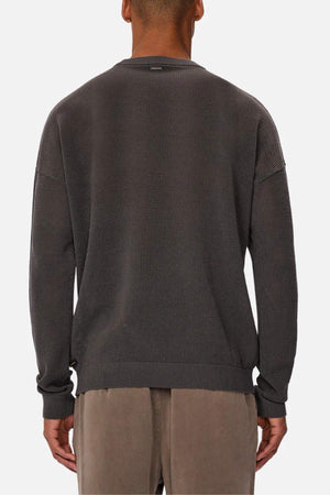 A person is shown from behind wearing the Industrie The Nanterre Crew Neck Knit, a textured dark gray oversized sweater, paired with light brown pants and standing against a plain white background.