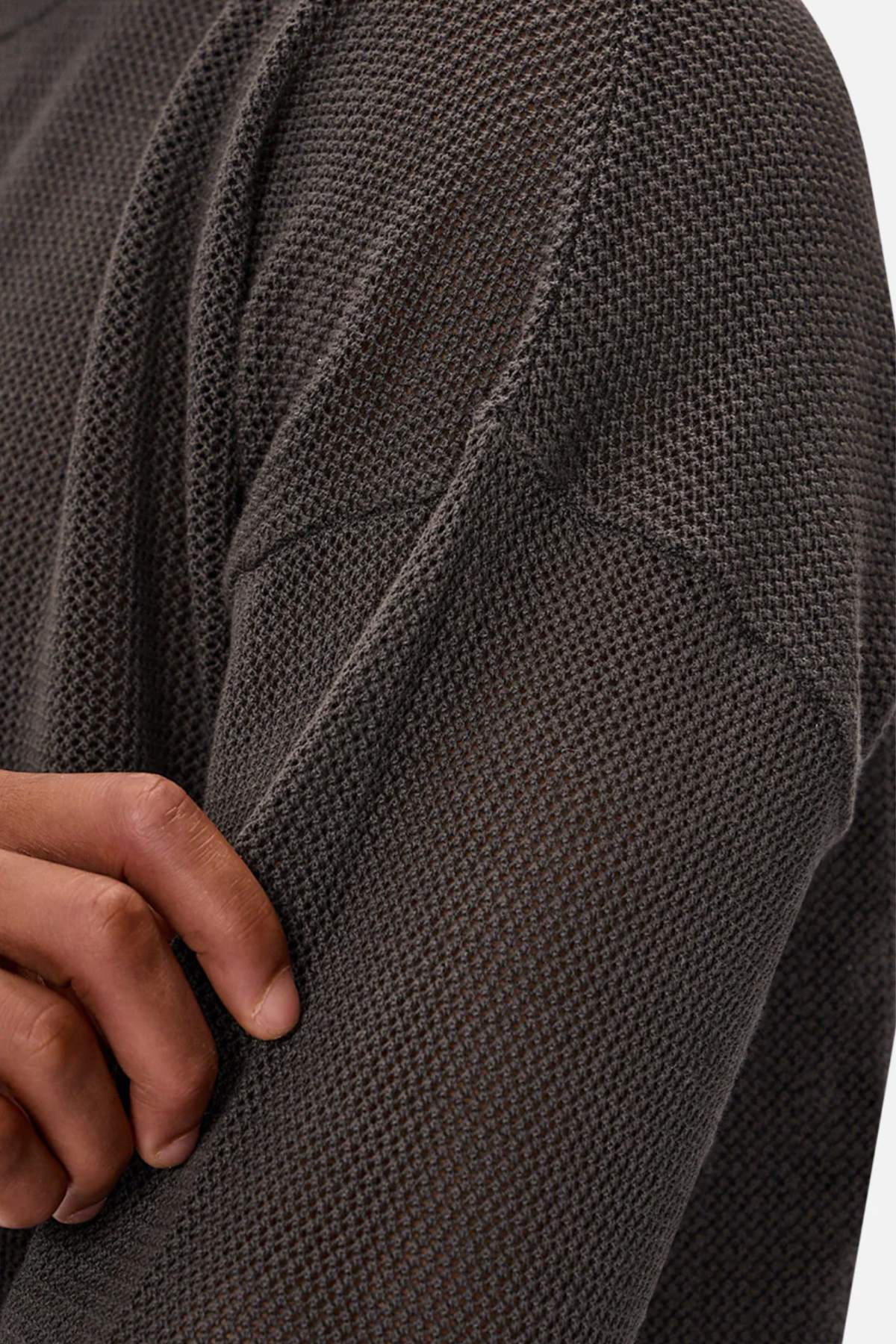A close-up shows a person wearing the Industrie The Nanterre Crew Neck Knit, a textured dark gray oversized sweater, gently pinching its fabric near the upper arm.