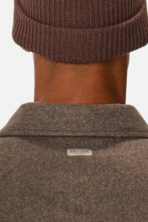 Close-up of the back of a person wearing Industrie The New Coleman Jacket in gray wool with a classic collar and small rectangular neck label, paired with a brown knit beanie. The jacket’s relaxed fit pops against the plain white background.