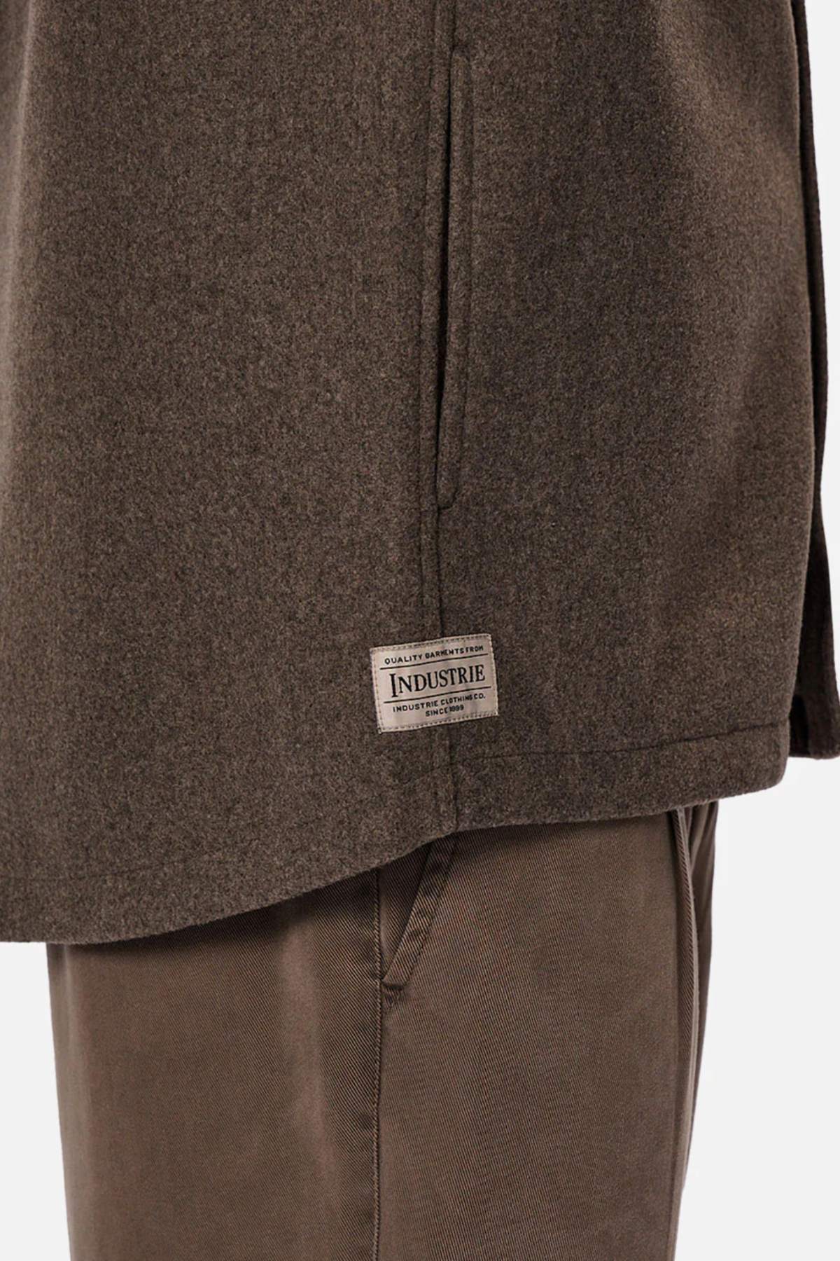Close-up of a person wearing the Industrie The New Coleman Jacket with brown pants. The relaxed fit jacket features a classic collar and a rectangular "INDUSTRIE" label near the hem. Background is plain white.