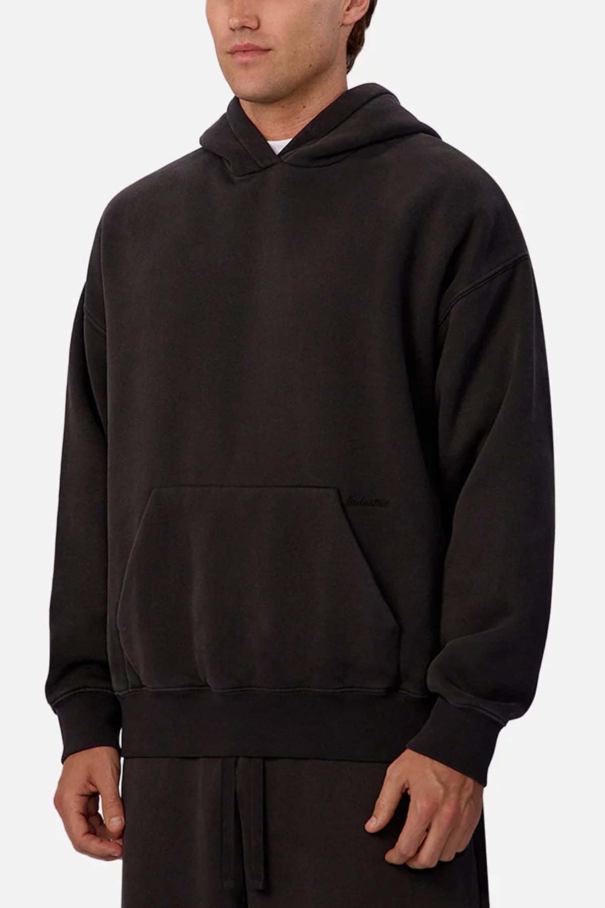 A person wears the Industrie The New Del Sur Fleece Hoodie in solid black, featuring an oversized fit with front pocket and hood. Only their torso and part of their face are visible against a plain light background, emphasizing the relaxed style.