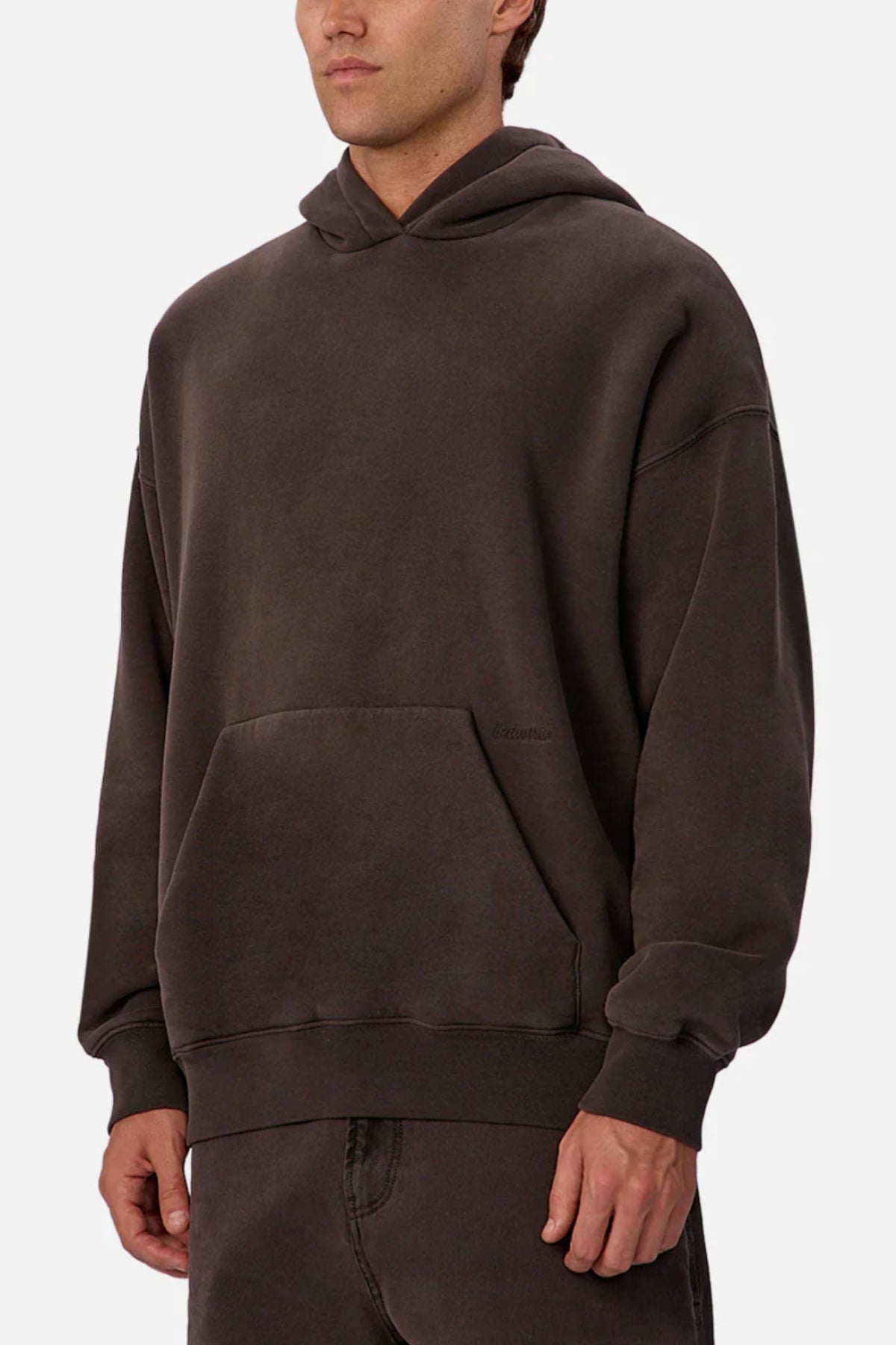 Someone wearing the Industrie The New Del Sur Fleece Hoodie—an oversized dark brown cotton-polyester hoodie with a front pocket—paired with matching pants, stands against a plain white background.