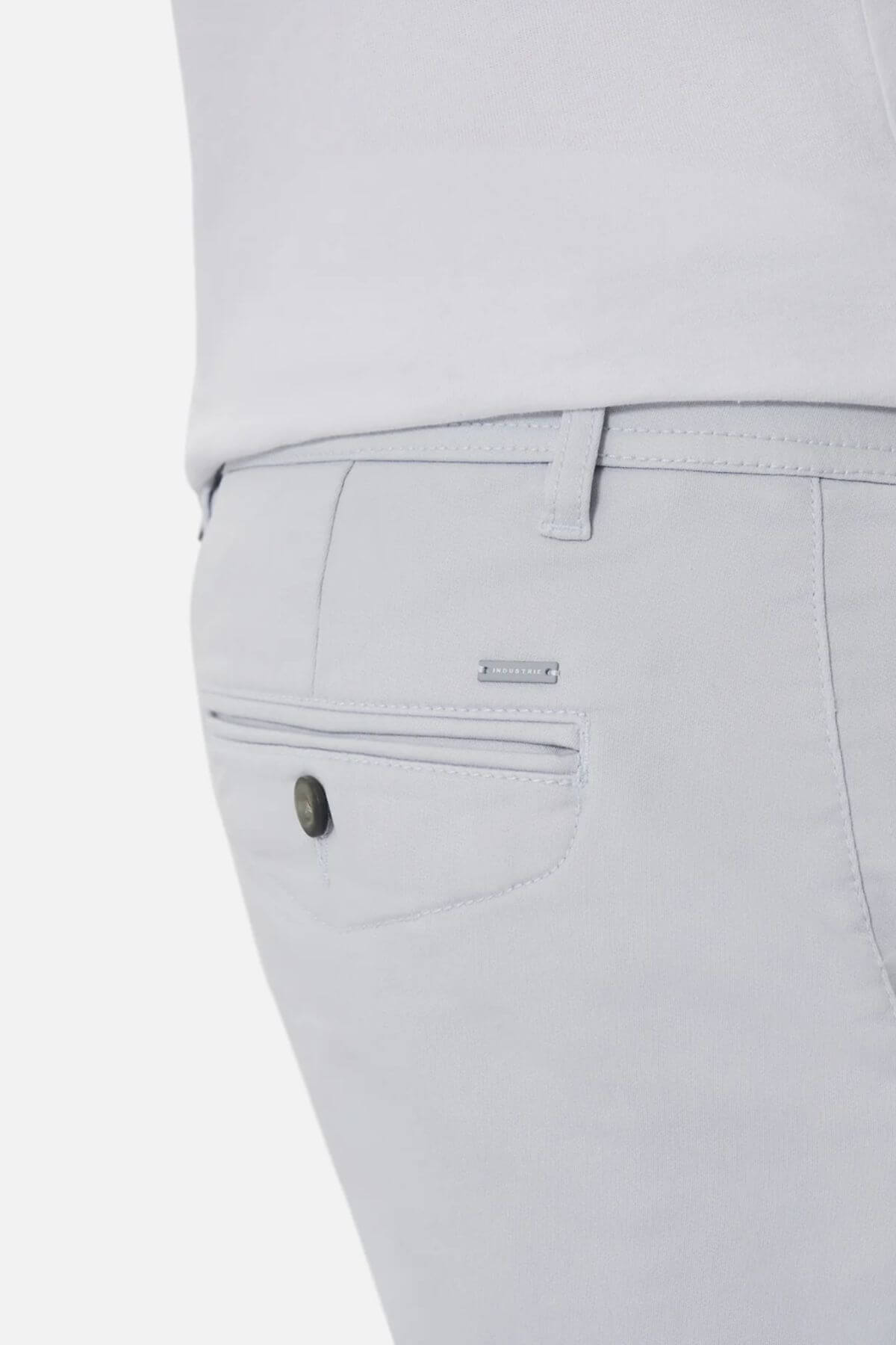 Close-up of the back pocket on light grey Industrie The New Drifter Cuba Short, featuring a single buttoned pocket and a metallic brand tag above it. The modern slim fit pairs comfortably with a white top for stylish wear.