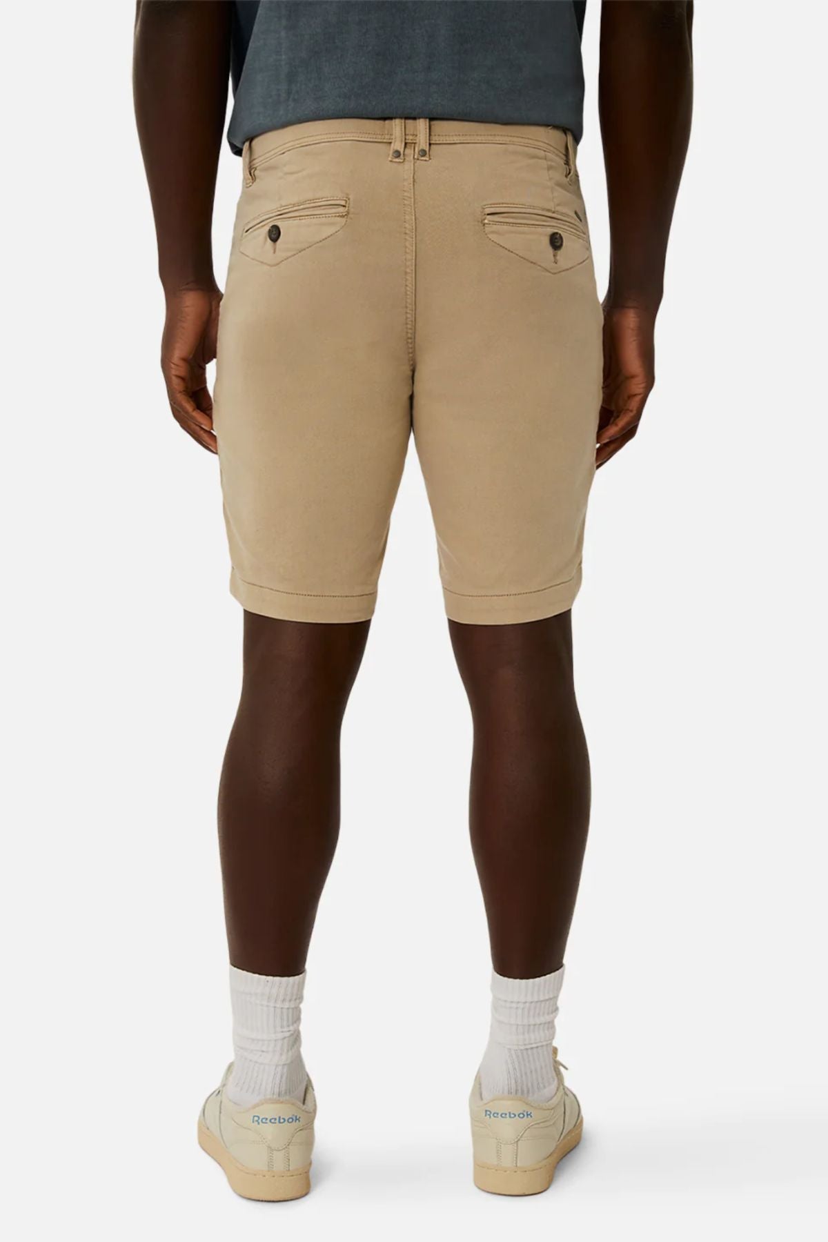 Rear view of a person wearing casual Industrie The New Drifter Cuba Shorts and a gray t-shirt, paired with white socks and beige sneakers. The plain, neutral background emphasizes the cool, relaxed vibe of their outfit.