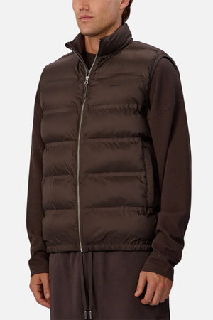 A man wears the Industrie The New Kyoto Puffer Vest, known for its featherlight feel, over a matching long-sleeve shirt and pants. The vest features horizontal quilting and a front zipper, styled against a plain light backgroundβideal for cool weather.