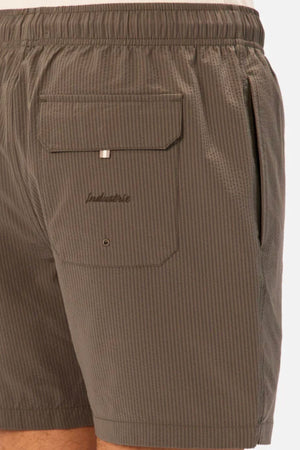 Close-up of a person wearing Industrie The New Seersucker Swim Short in brown seersucker with an elastic waistband, side pocket, and a large flap-and-button back pocket embroidered with "Industrie.