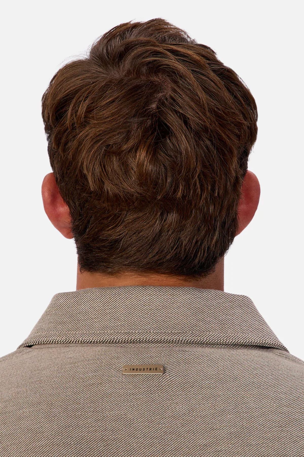 A man with short, wavy brown hair is seen from behind in a beige Industrie The New Westport Jacket featuring a small metallic โINDUSTRIEโ tag on the back collar, set against a plain white background.