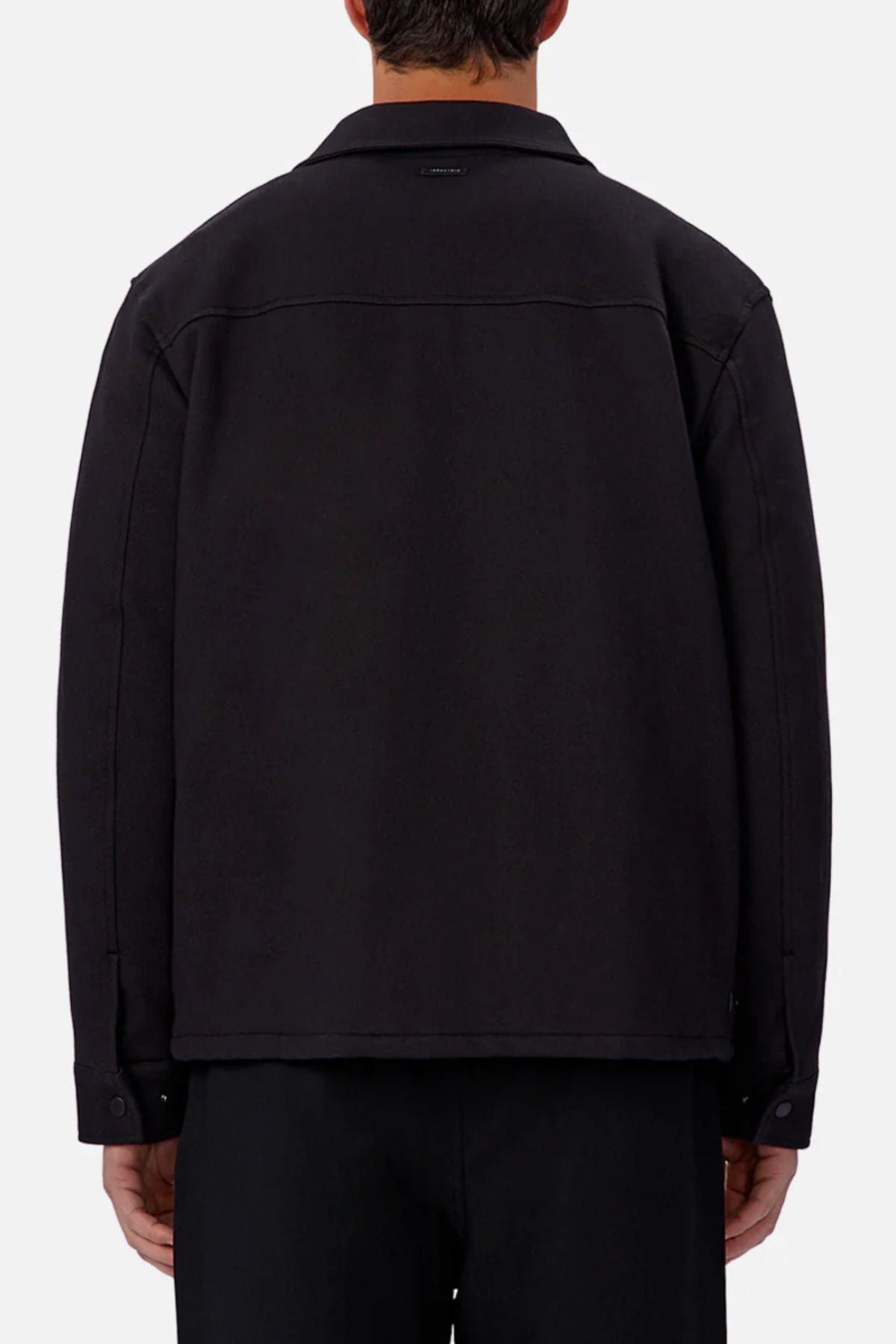 A person is seen from behind wearing the Industrie The New Westport Jacket in black with matching pants. The loose, long-sleeve smart-casual jacket contrasts against a plain light background.