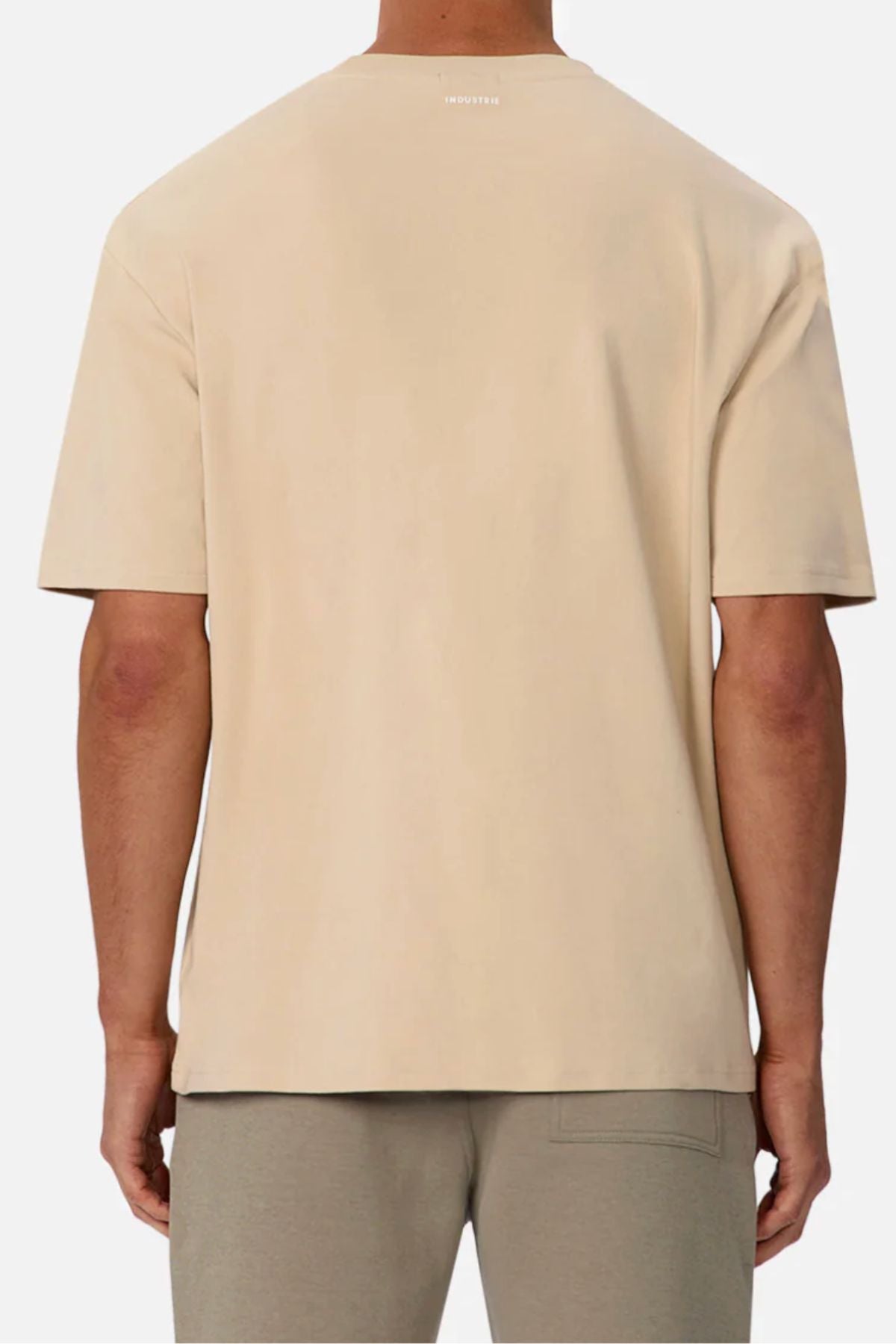 A person is shown from the back wearing the Industrie The Newport Tee in an oversized, short-sleeve beige style with light gray pants against a plain background.