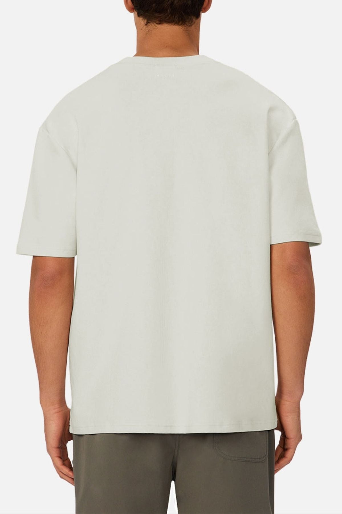 A person is shown from the back, wearing an oversized fit, light-colored Industrie The Newport Tee with short sleeves and dark shorts against a white background.