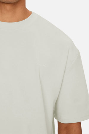 A close-up of a person wearing the Industrie The Newport Tee, a heavy weight, light beige t-shirt with short sleeves, oversized fit, minimal design, and subtle "INDUSTRIE" text near the chest.