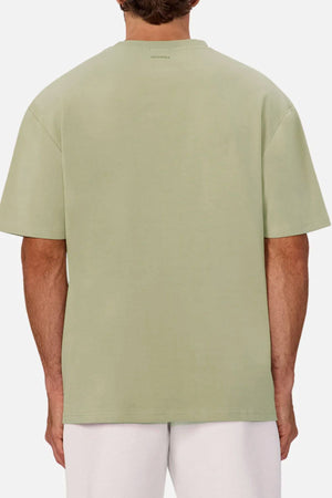 A person is shown from the back wearing the Industrie The Newport Tee, an oversized heavyweight light green T-shirt, paired with white shorts against a plain light background.