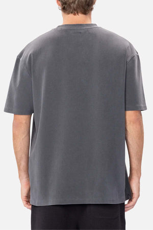 A person with short brown hair wears an oversized charcoal gray Industrie The Newport Tee, made of 100% cotton with a soft, slightly worn texture. They stand against a plain white background.