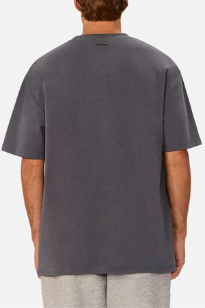 A person wearing an oversized fit, dark gray Industrie The Newport Tee and light gray shorts is pictured from the back. The 100% cotton T-shirt has a simple design with no visible logos or graphics on the back. The background is plain white.