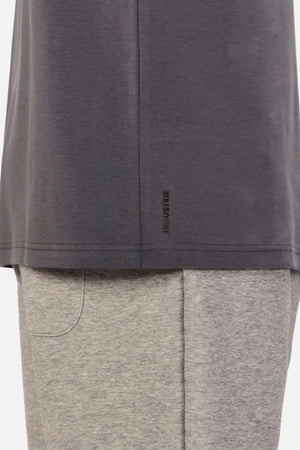 Close-up of a person wearing an oversized fit, dark grey Industrie The Newport Tee with a small logo near the hem, paired with light grey shorts. The image highlights the lower half of the 100% cotton shirt and the upper portion of the shorts.