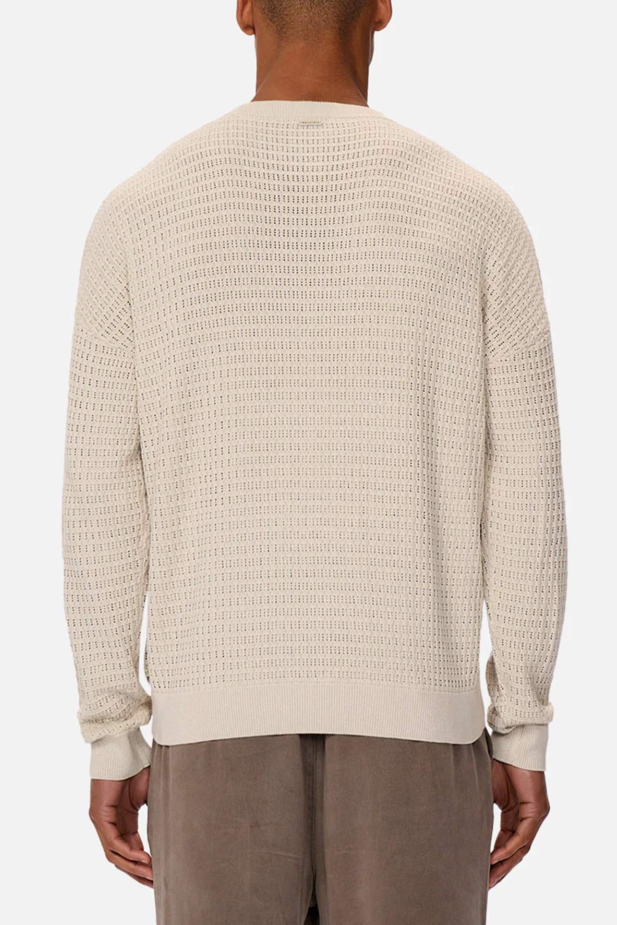 Back view of a person wearing Industrie The Nunez Long Sleeve Knit, a cream-colored, 100% cotton sweater with a small square pattern and a loose fit, paired with taupe pants against a plain white background.