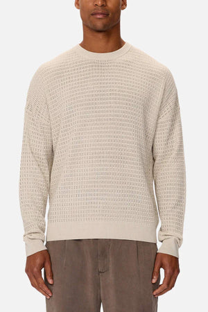 Someone is wearing the Industrie The Nunez Long Sleeve Knit, a textured beige sweater made from 100% cotton. It has long sleeves and a round neckline, paired with light brown trousers. The subtle pattern design contrasts beautifully against the plain white background.