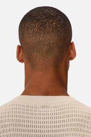 The image shows the back of a person's head with short hair, wearing an Industrie The Nunez Long Sleeve Knit top. The garment is light-colored and made from 100% cotton, set against a white background that highlights its texture.