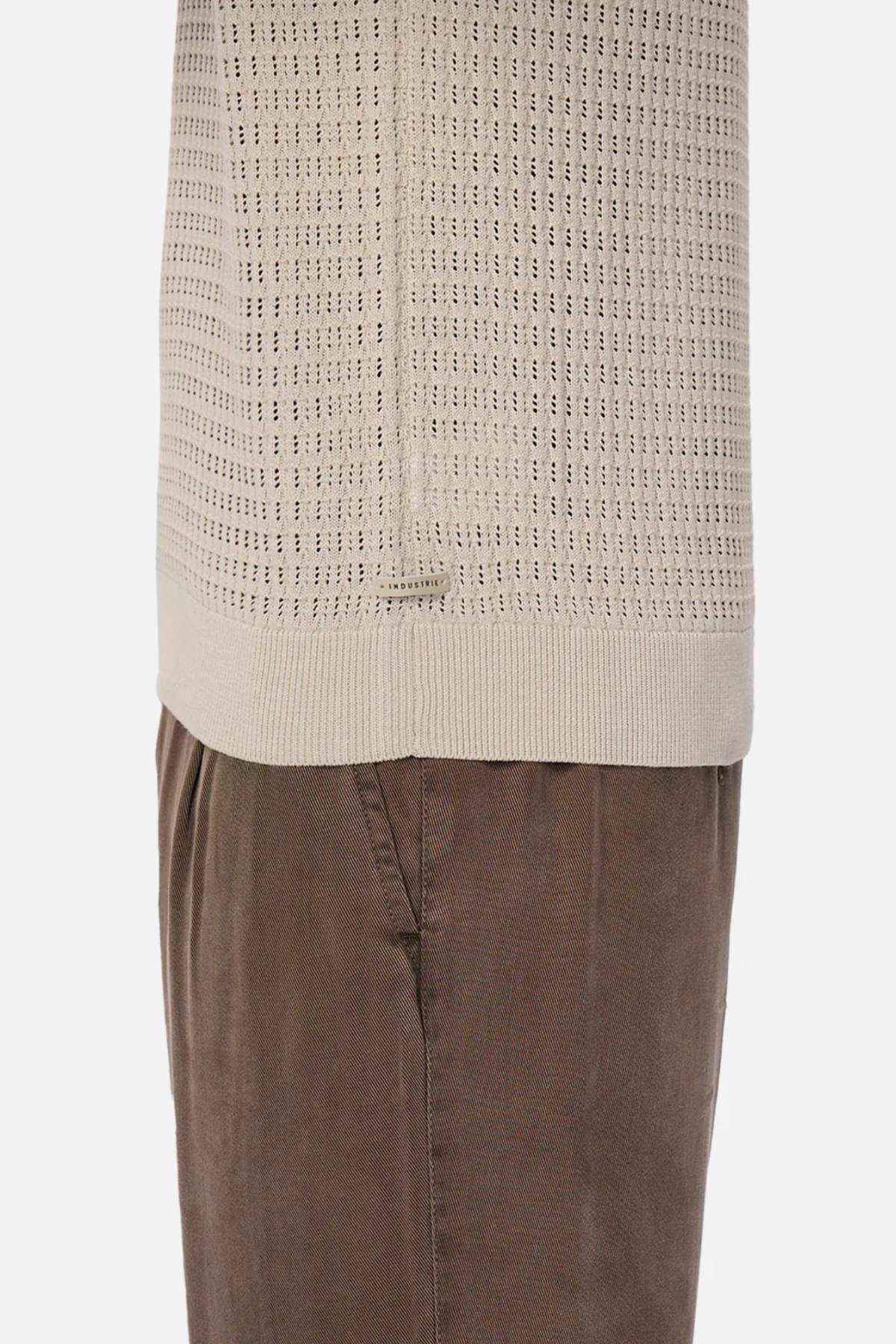 A close-up side view shows someone wearing a beige Industrie The Nunez Long Sleeve Knit sweater paired with brown corduroy pants, highlighting the intricate design and 100% cotton texture.