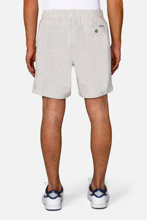 A person faces away from the camera, wearing Industrie The Ortenza Short in light gray with an elastic waistband, textured fabric, and a single buttoned back pocket, paired with a white shirt and white sneakers with blue accents.