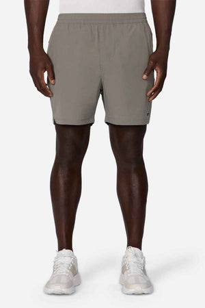 A person wearing Industrie The Owens Short in gray, crafted from quick-drying fabric, and white sneakers stands against a plain white background. The image shows a partial view from the waist down, emphasizing the shorts' above-knee length and comfortable elasticized waistband.