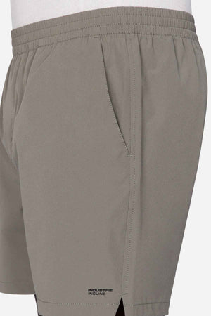 A close-up of a person wearing "Industrie The Owens Short" in light gray, featuring an elasticized waistband and the branding "Industrie Incline" near the hem. These above-knee-length shorts boast quick-drying fabric and have a visible side pocket. The person is sporting a white shirt that is slightly tucked in.