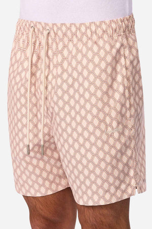 A person wearing Industrie The Panama Swim Short in light pink with a geometric hexagonal pattern, white drawstrings, and an elastic waistband—stylish men’s swimwear designed for quick-dry comfort.