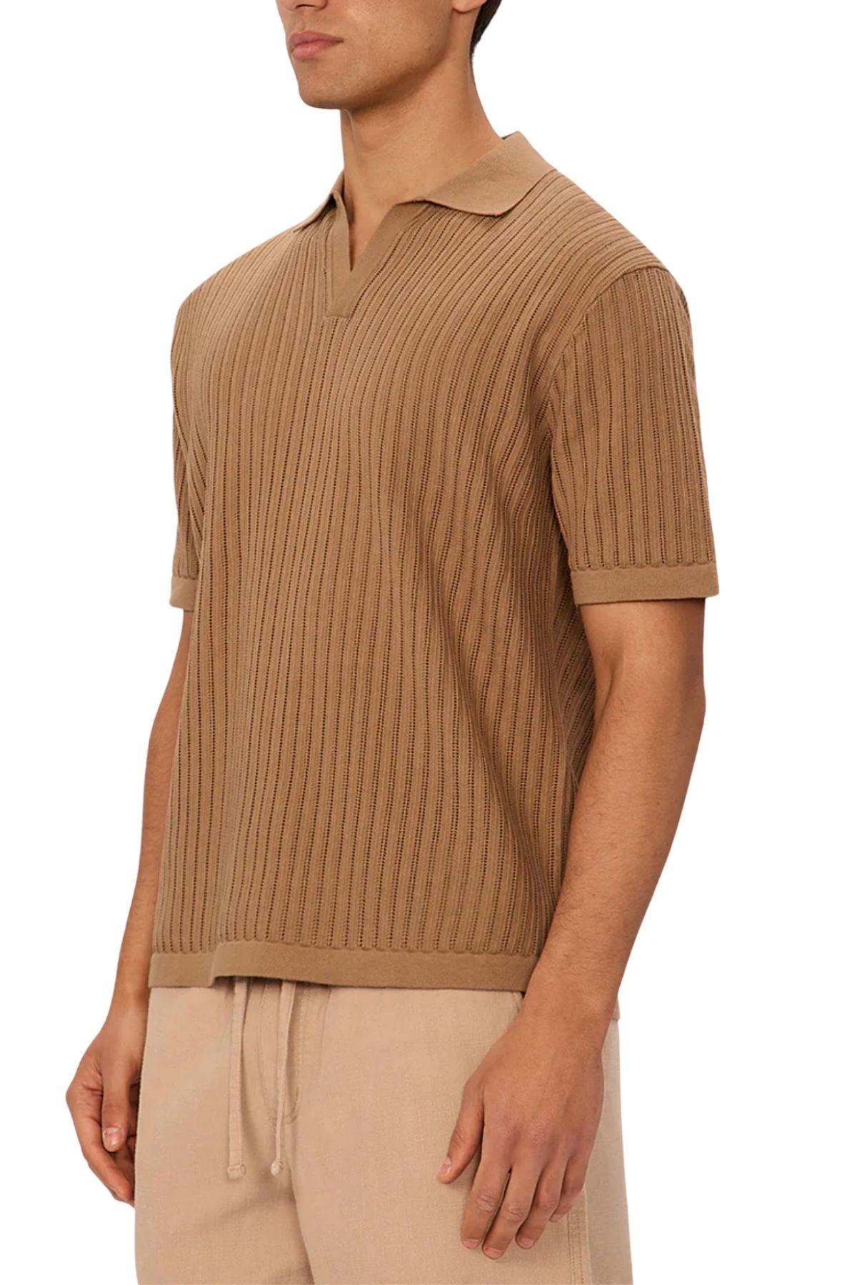 A man stands against a plain white background, wearing the Industrie The Poolside Polo in camel ribbed cotton with short sleeves and a split collar, paired with light beige drawstring pants.