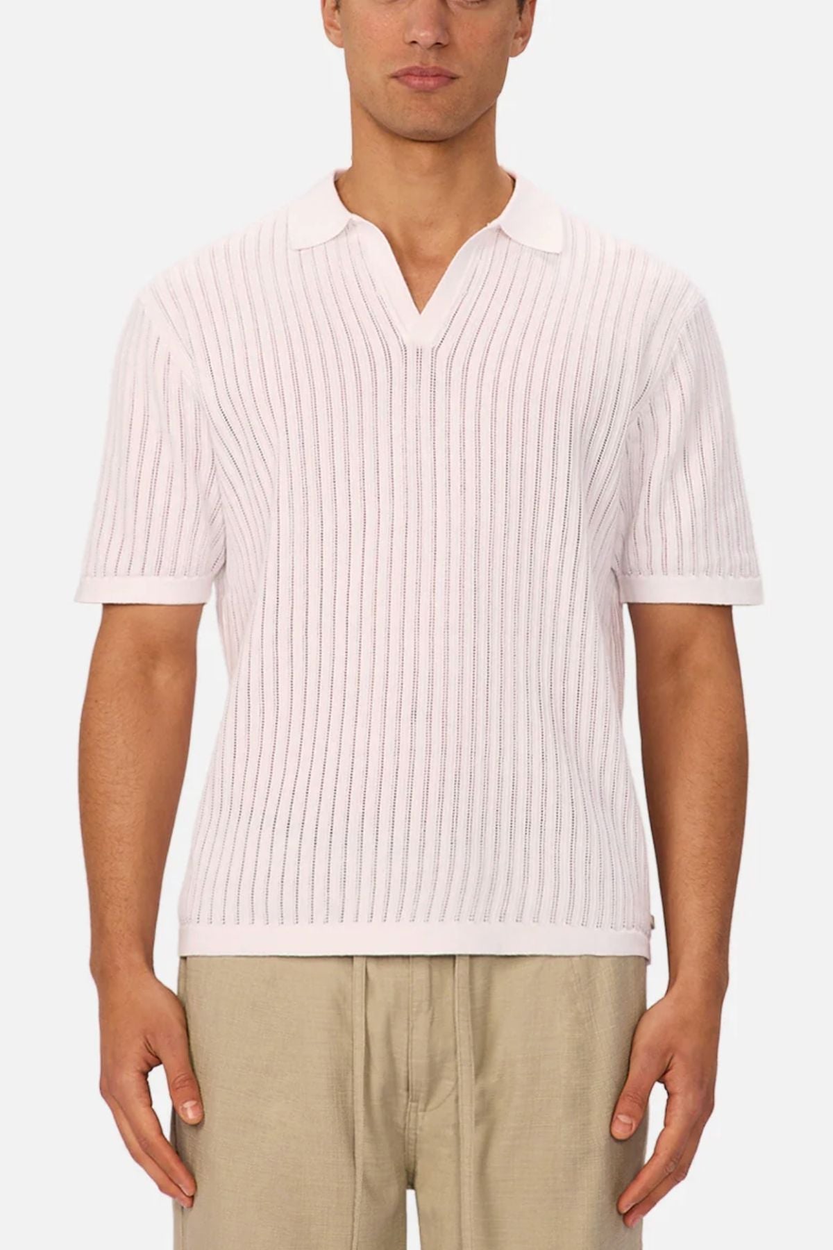 A man wears the Industrie The Poolside Polo—a white, short-sleeve cotton knit with a split collar—paired with light beige pants, standing against a plain background for an effortlessly casual look.