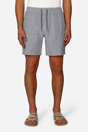 A person wearing Industrie The Portico Linen Short in gray, paired with a white top and beige sandals, stands against a white background. These shorts, perfect for a summer wardrobe, feature a drawstring waist. The focus remains on the lower half of the body.