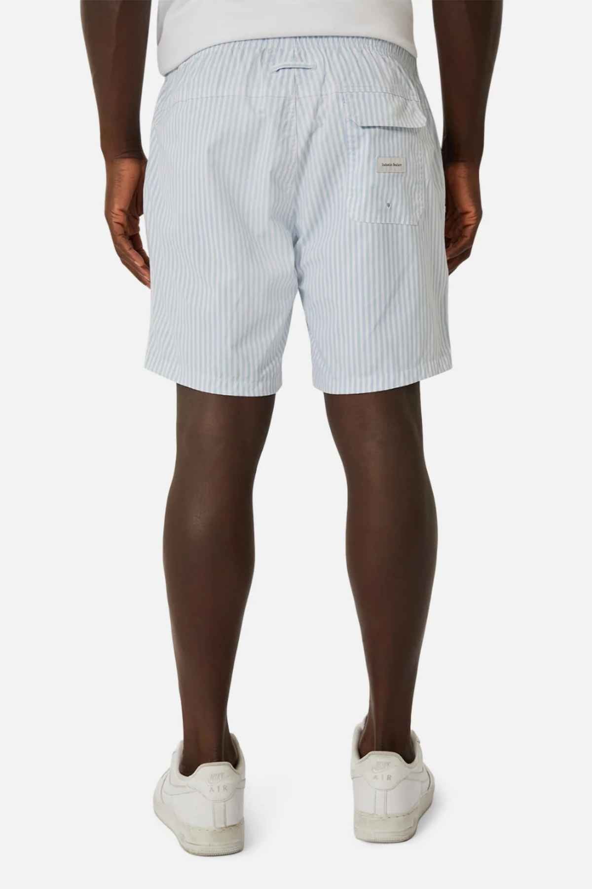 A person is seen from behind wearing Industrie The Princeton Bahama Short in light blue and white stripes, paired with white sneakers. These shorts, crafted from a comfortable fabric blend, feature a small pocket on the right side. The setting is a plain white background.