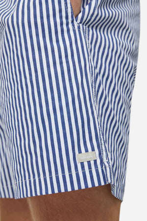 Close-up of a person wearing Industrie The Princeton Bahama Short, featuring a blue and white vertical stripe pattern. The comfortable fabric blend has a textured finish, highlighted by a small white label on the side seam. The background is plain and blurred.