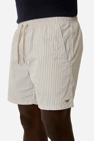The individual showcases Industrie The Princeton Bahama Short, which presents cream and beige vertical stripes. It features an elastic waistband with a drawstring, while the pockets are subtly adorned with Industrie branding against a solid white background.