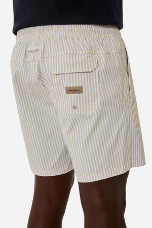 An individual is wearing Industrie The Princeton Bahama Shorts in a light color, featuring vertical stripes and an elastic waistband. These shorts are detailed with a back pocket adorned with a button flap, subtly showcasing the Industrie branding.