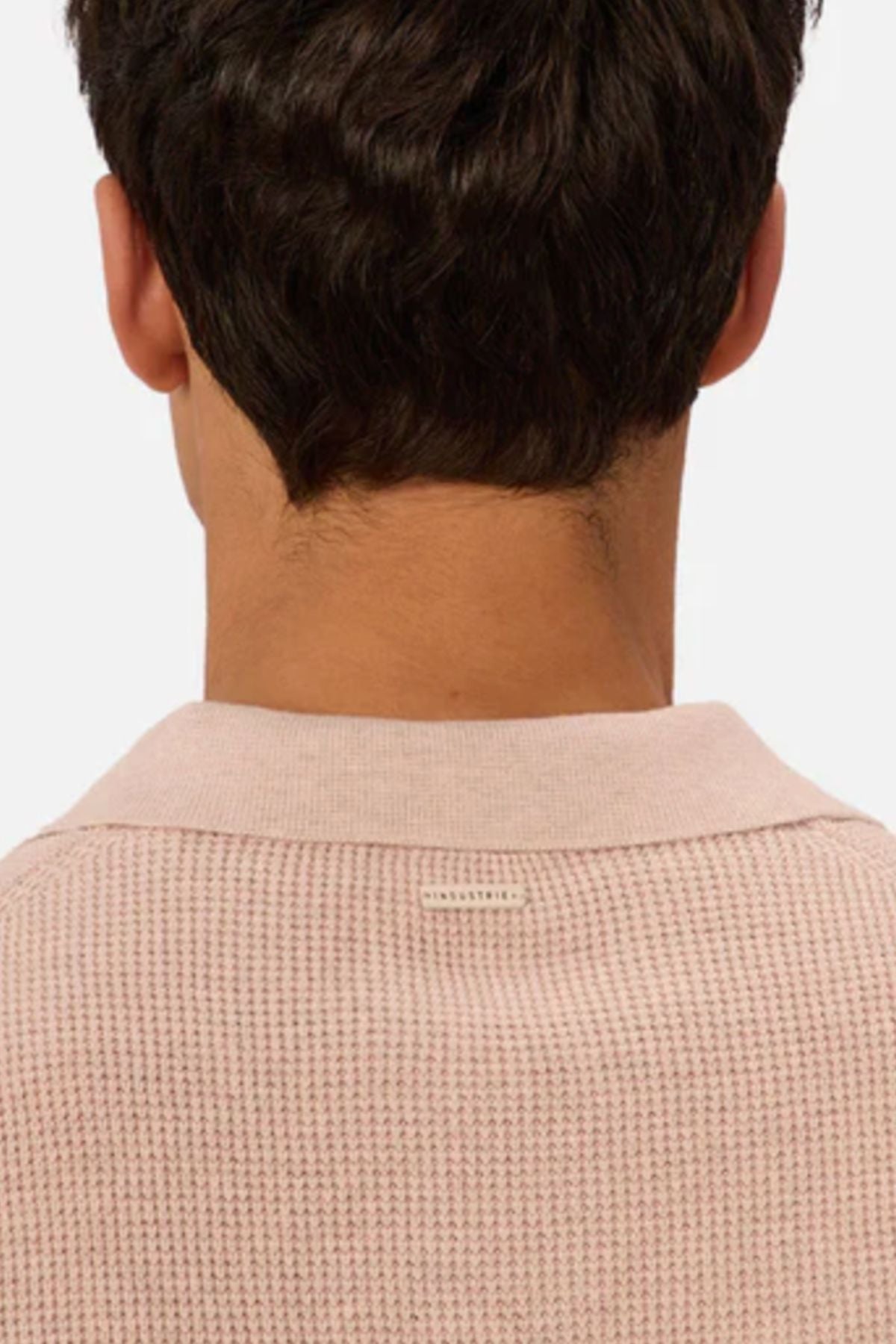 A person with short, dark hair is seen from behind wearing the Industrie The Ravenna Polo, a light pink textured waffle knit polo with a collar, set against a plain, light background.